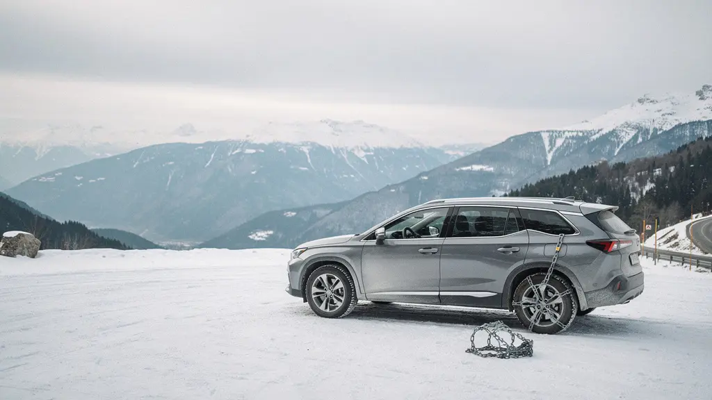 SUV familial garé au bord d’une route de montagne enneigée avec un ciel dégagé et beaucoup d’espace vide autour.